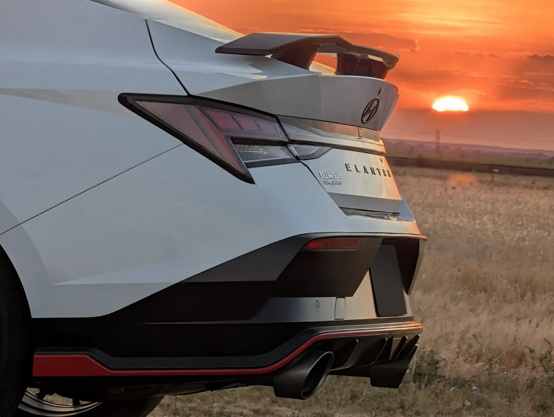 Factory rear wing, diffuser, and dual exhaust at sunset; license plate redacted